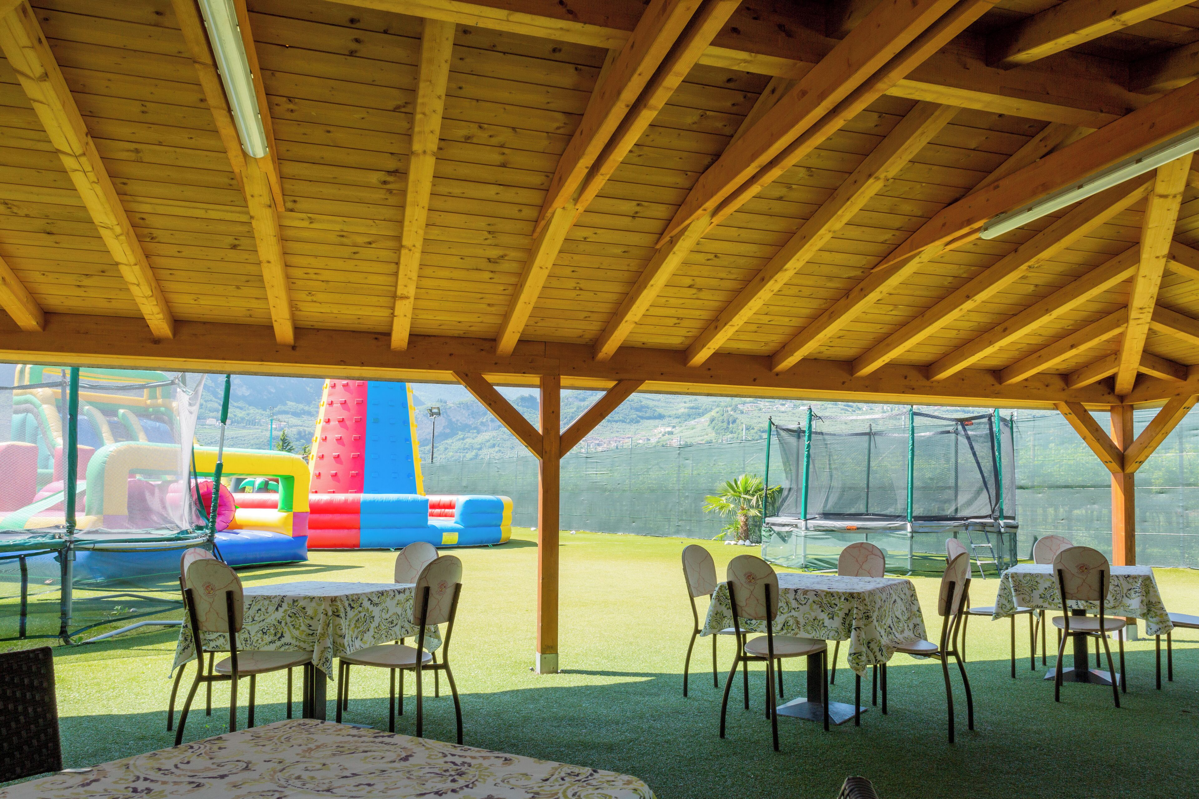 Un espacio al aire libre cubierto con mesas y sillas, un trampolín y vistas al exterior.