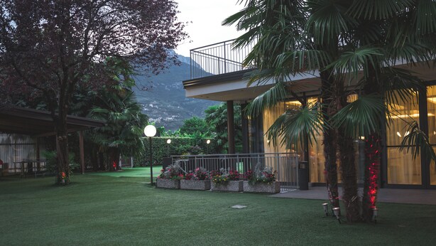 A modern building with a balcony, surrounded by a well-maintained garden with various plants and flowers.