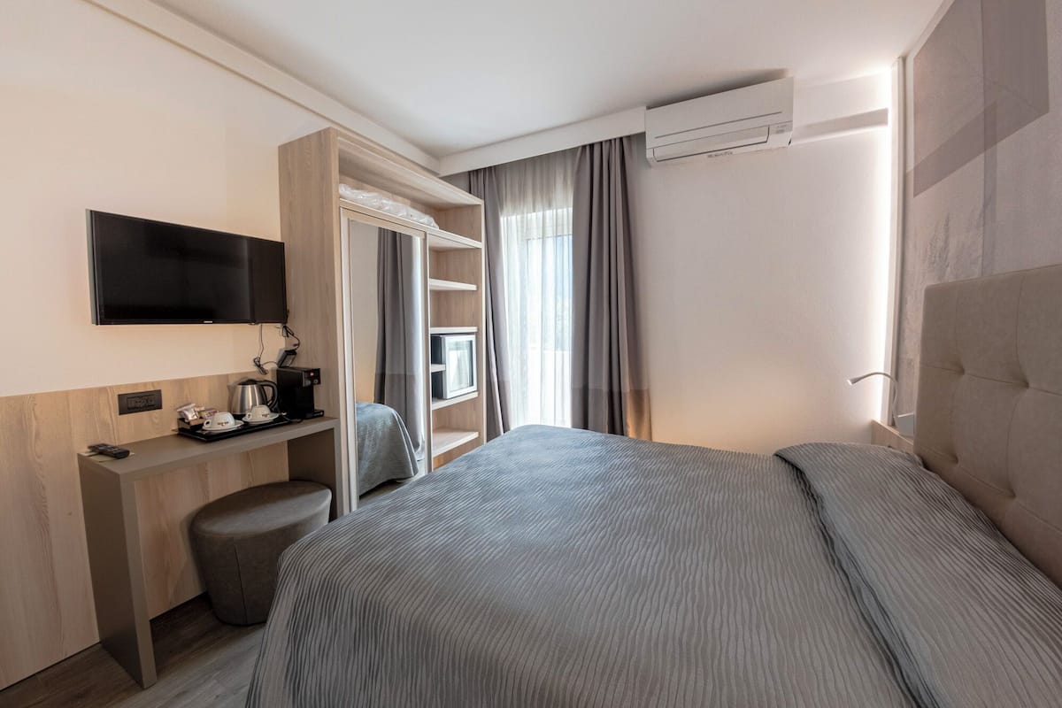 Een moderne hotelkamer met een bed, een bureau met koffiezetapparaat, een televisie en een kledingkast.