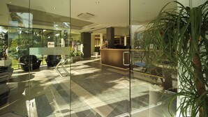 A reception area with a glass partition, a reception desk, seating area, and potted plants.