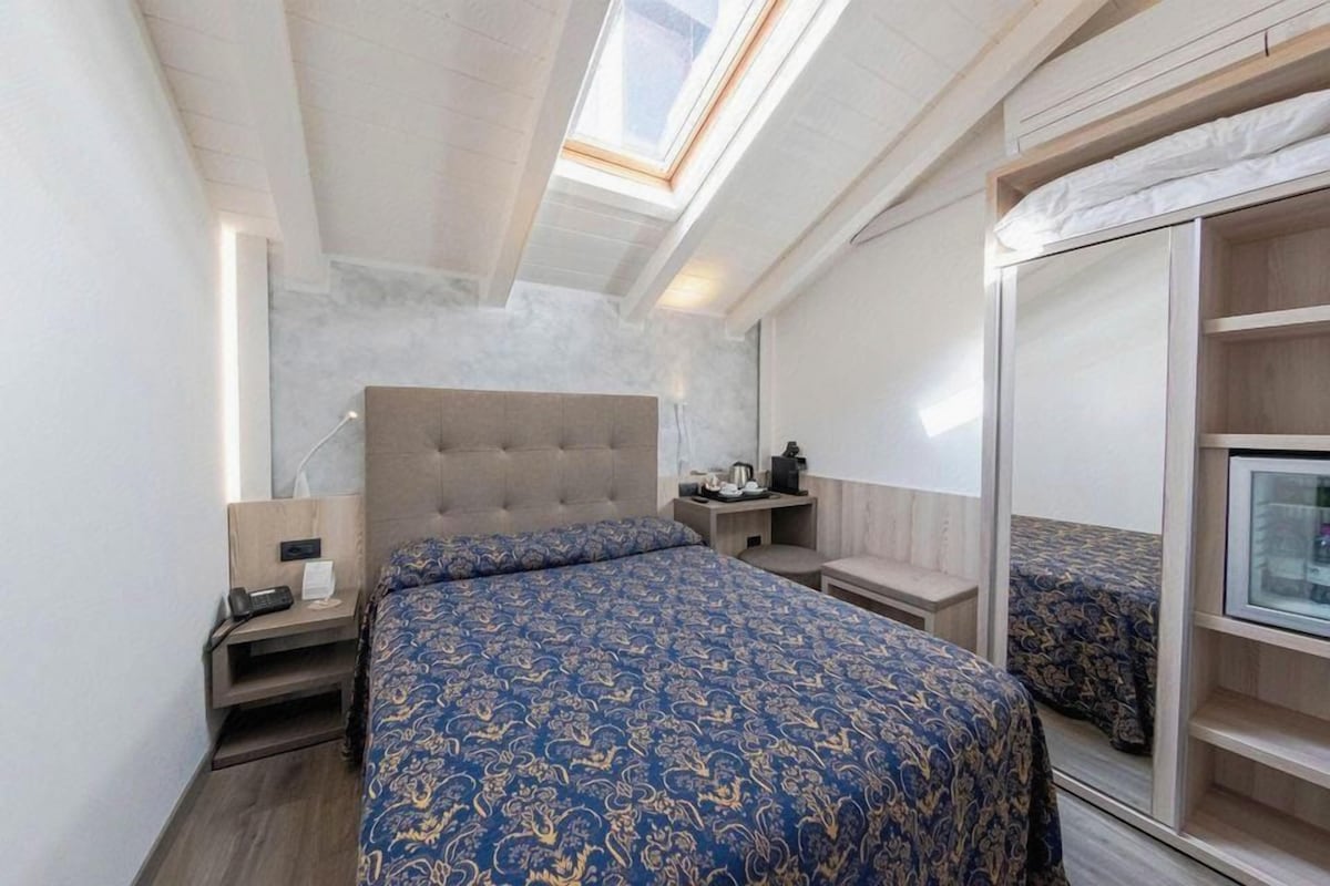 Une chambre à coucher avec un grand lit, une table de chevet, une commode, une armoire et un puits de lumière.