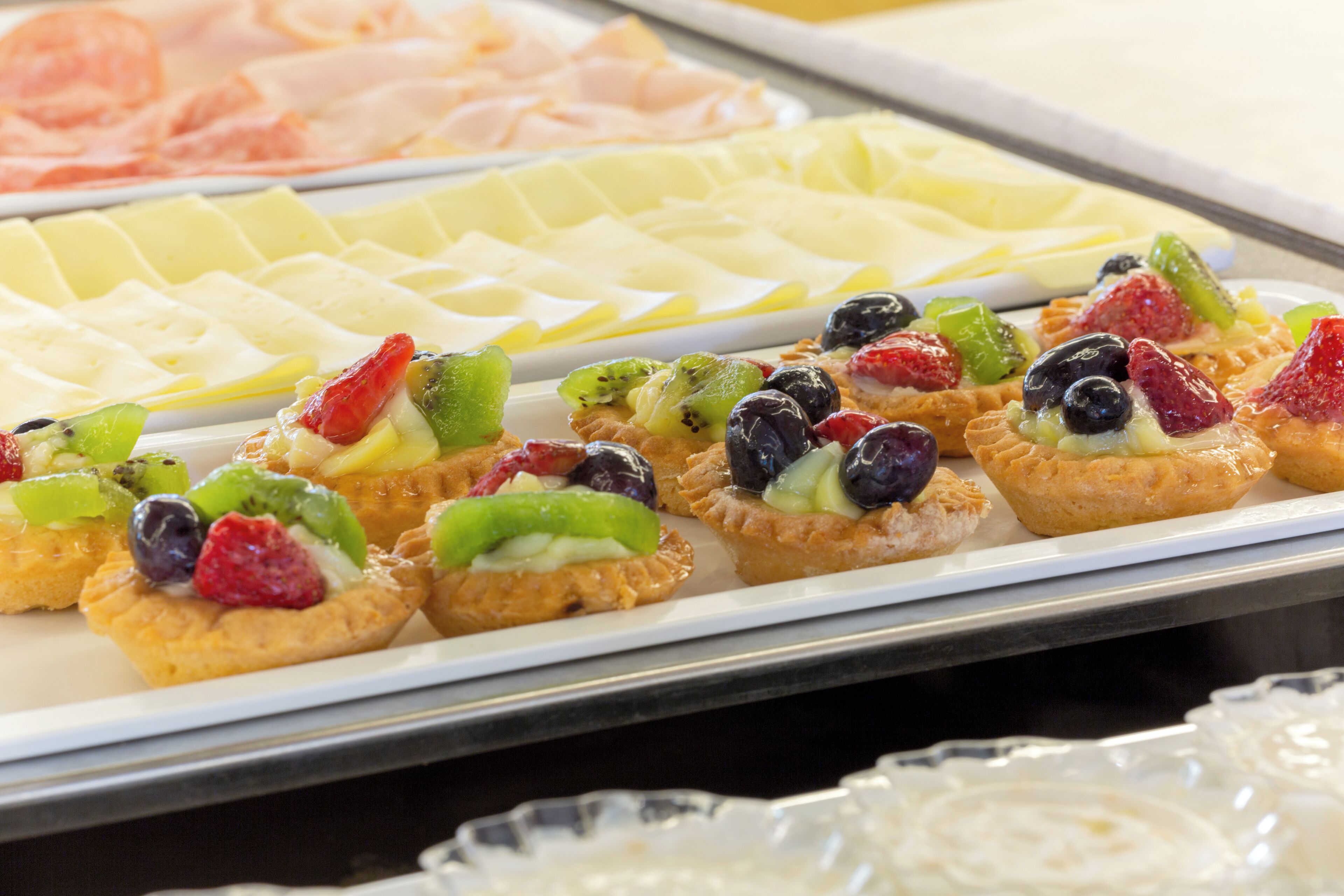 Un bufé con diversos alimentos, incluyendo pasteles coronados con frutas.