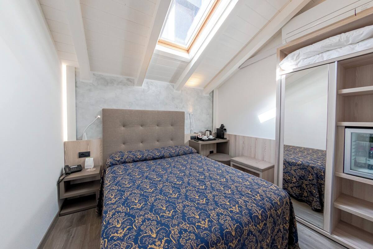 Een slaapkamer met een bed, nachtkastje, lamp en spiegel.