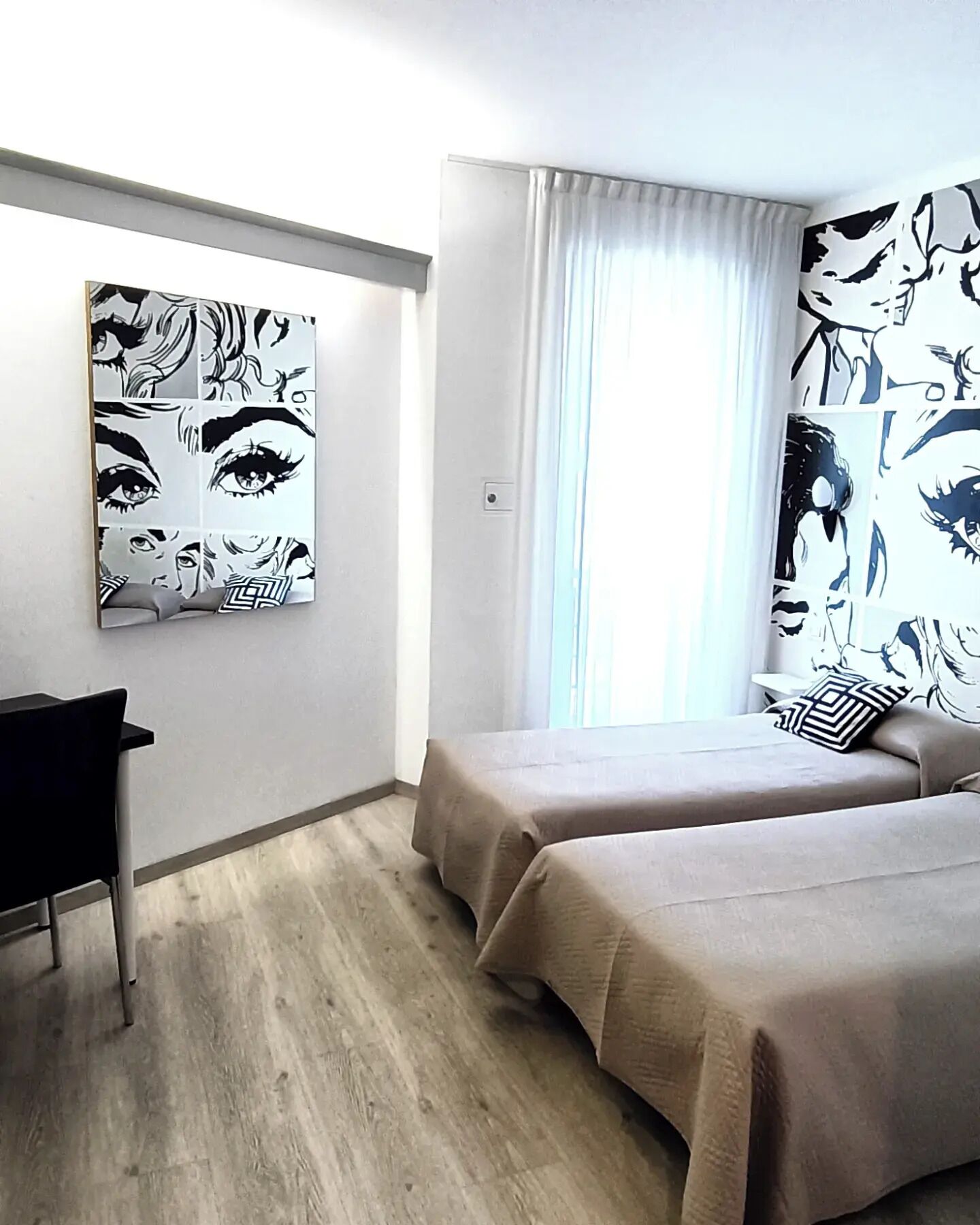 A hotel room with two beds, a desk, and artwork on the walls.