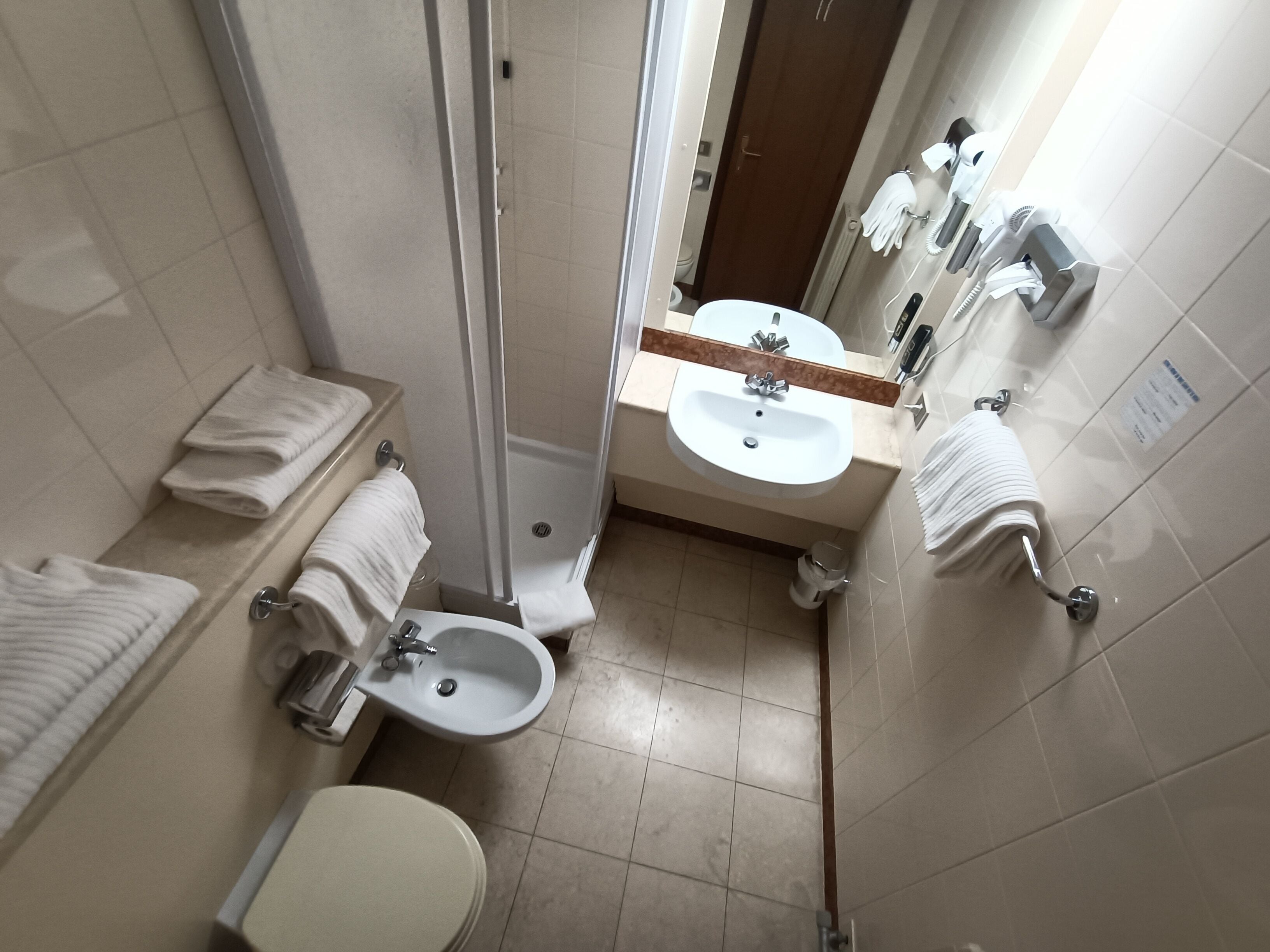 A compact bathroom with a toilet, bidet, sink, and shower. Towel racks are available for convenience.
