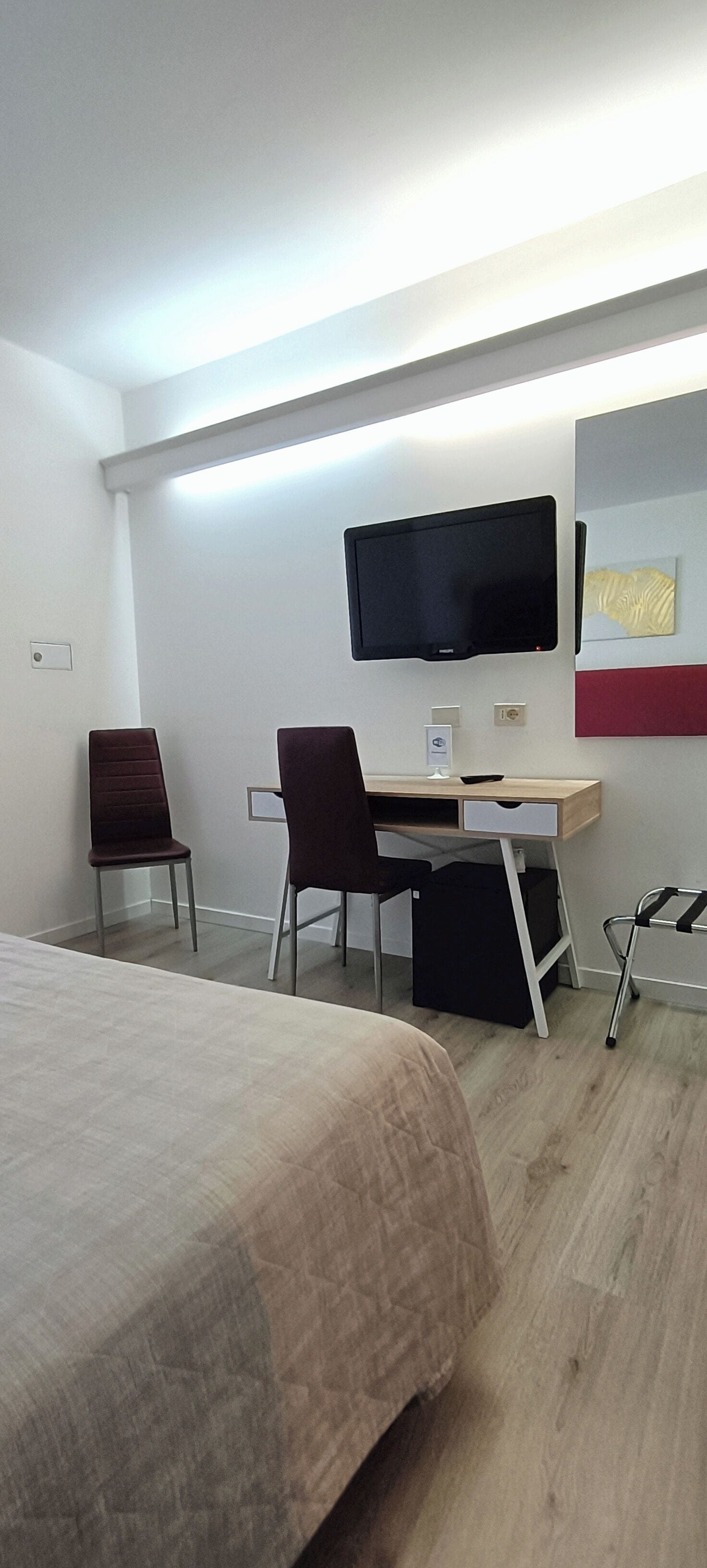 Hotelkamer met een bed, een bureau met stoel, een aan de muur bevestigde televisie en een rolstoel.
