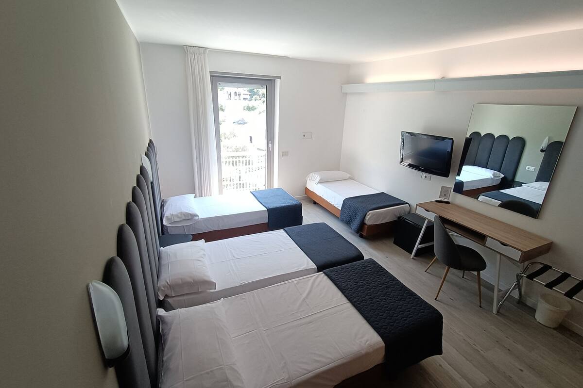 Une chambre d’hôtel avec deux lits simples, un bureau, une chaise, une télévision et un grand miroir.