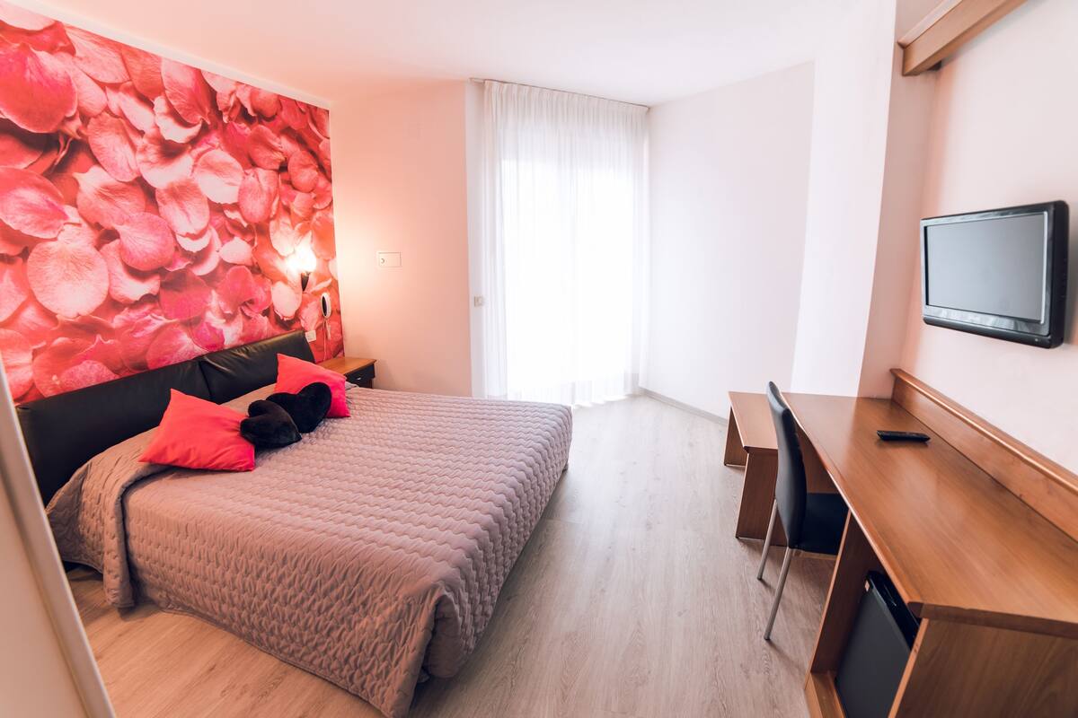 Une chambre à coucher comprenant un lit, un bureau, une télévision et un mur orné d’un motif floral.