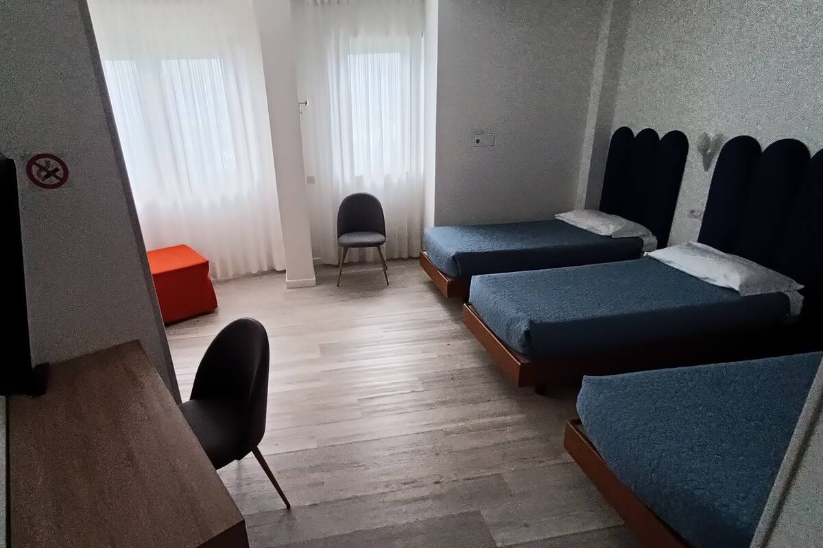 Une chambre avec deux lits, une chaise, un bureau et un pouf rouge.
