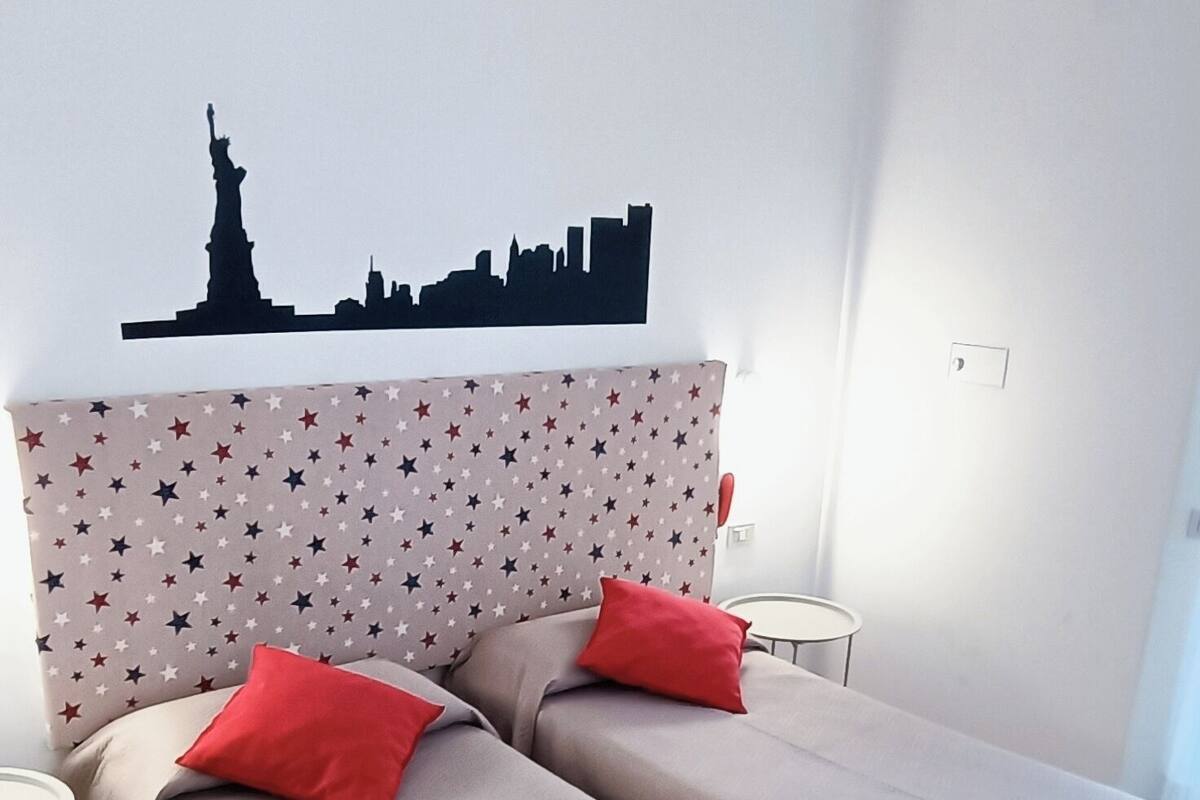 Une chambre d’hôtel avec deux lits simples, une décoration murale représentant le panorama de la ville, une tête de lit ornée d’un motif étoilé et un plancher en bois.