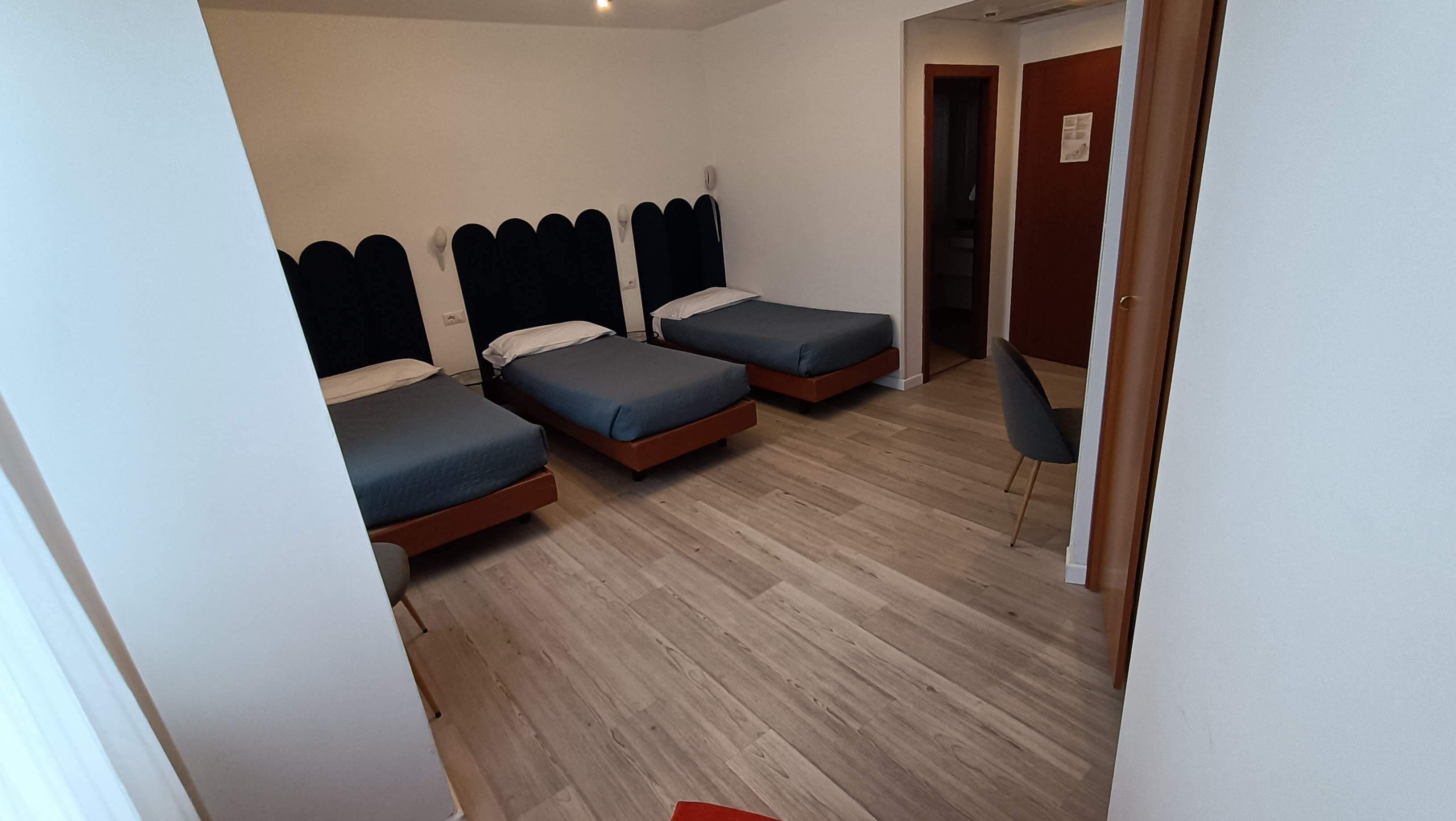 A room with three beds, a wooden floor, and a chair.