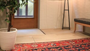 A room with a wooden door, a potted plant, a floor lamp, a bench, and a patterned rug. - Hotel Bridge (Venice)