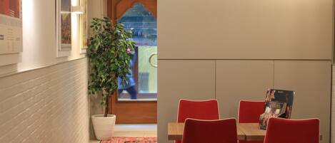A dining area with a table and red chairs, a potted plant, and a patterned rug.