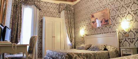 A bedroom with a bed, a desk, and a chair. There is a chandelier on the ceiling and a painting on the wall.