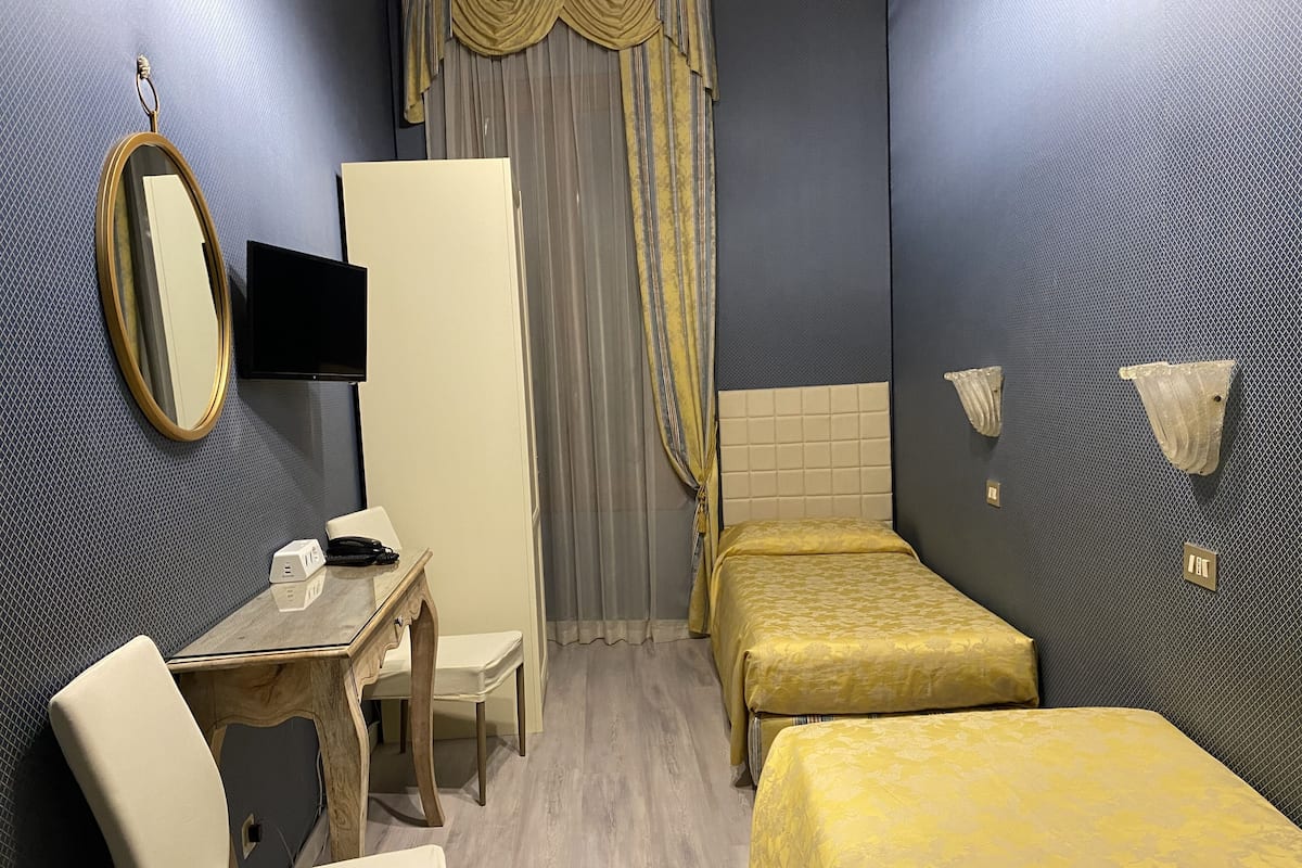 Hotellihuone, jossa on työpöytä, kaksi erillistä sänkyä, televisio ja peili.