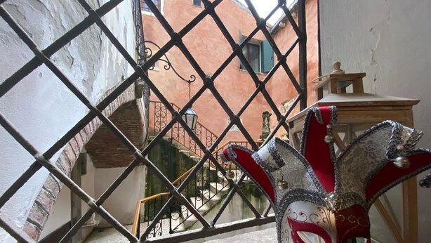 A Venetian mask with a red and white design, placed on a stone ledge. - Hotel Bridge (Venice)