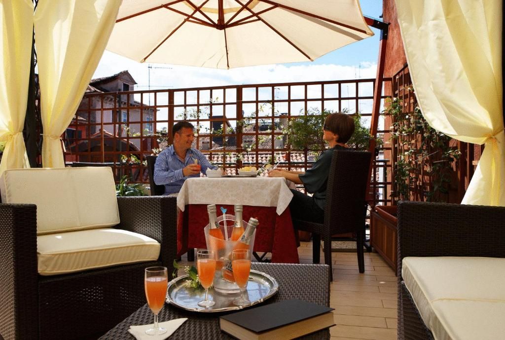An outdoor seating area with wicker furniture, a table with a tray of drinks, and a view of buildings in the background.