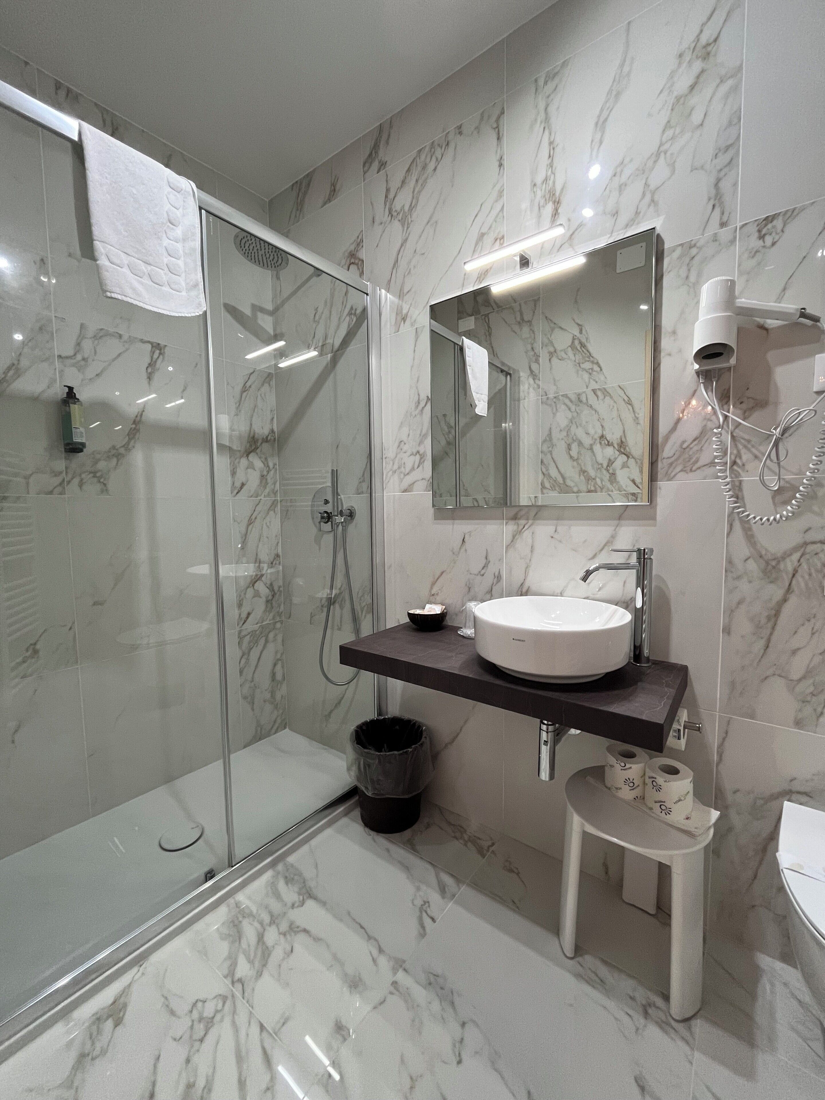 A modern bathroom with a glass-enclosed shower, a white sink, and a mirror above it.