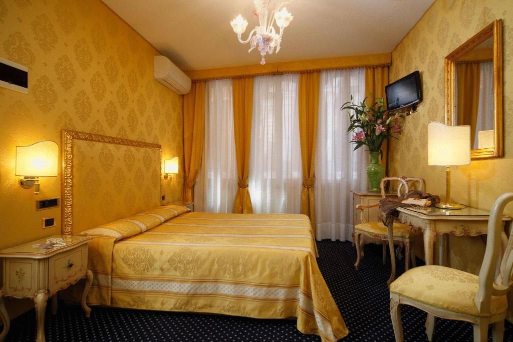 A hotel room with a bed, a desk with a chair, a television, and a mirror.