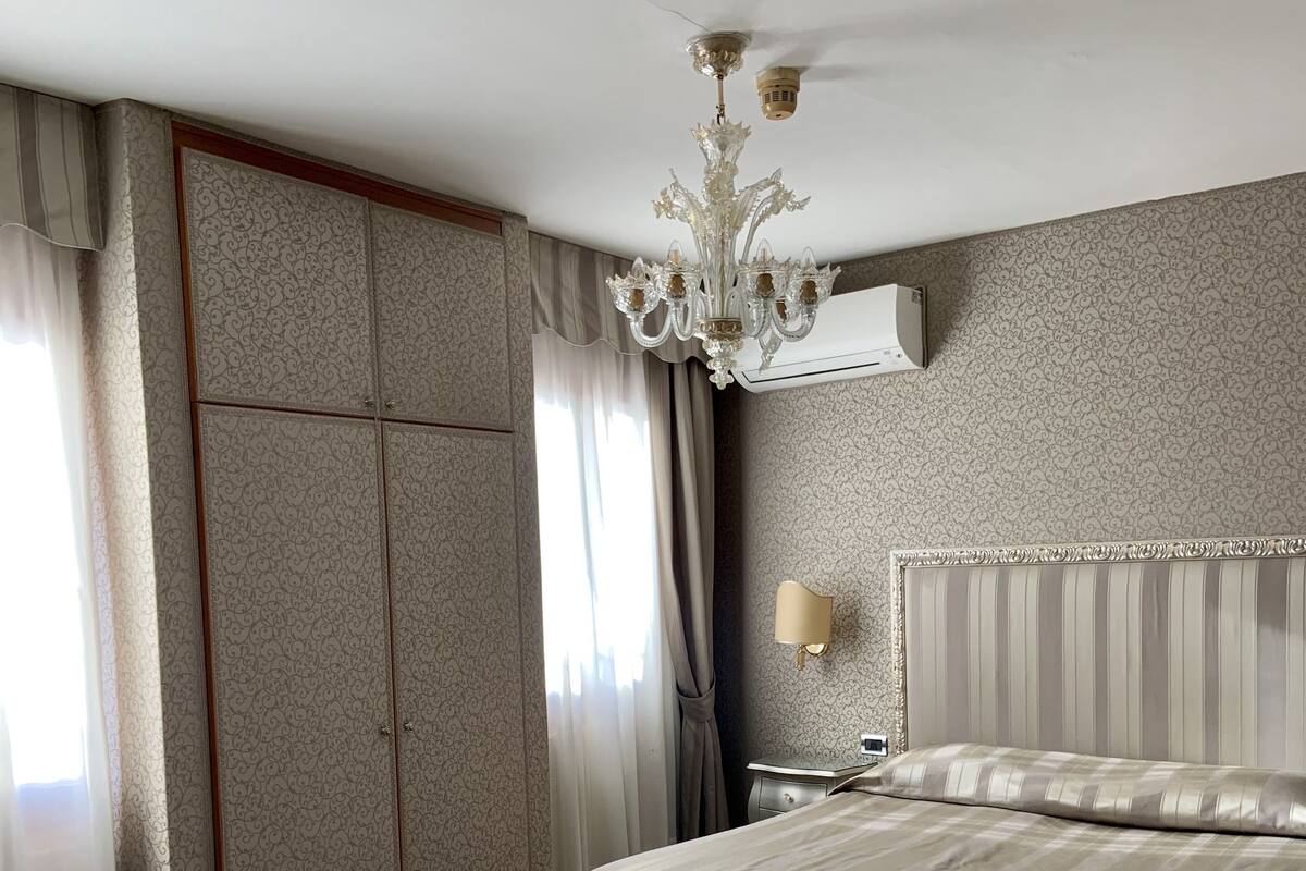 A hotel room with a bed, a desk, a chair, a wardrobe, and a chandelier.
