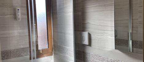 Un baño moderno con ducha de vidrio, inodoro blanco y lavamanos de mármol.