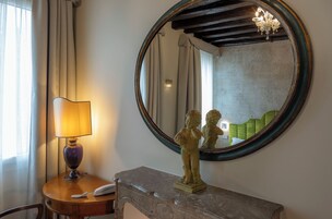 Quarto com espelho redondo, abajur, telefone e uma estátua sobre uma mesa de mármore.