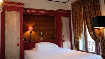 A hotel room with a bed, a nightstand, a lamp, and a window with curtains.