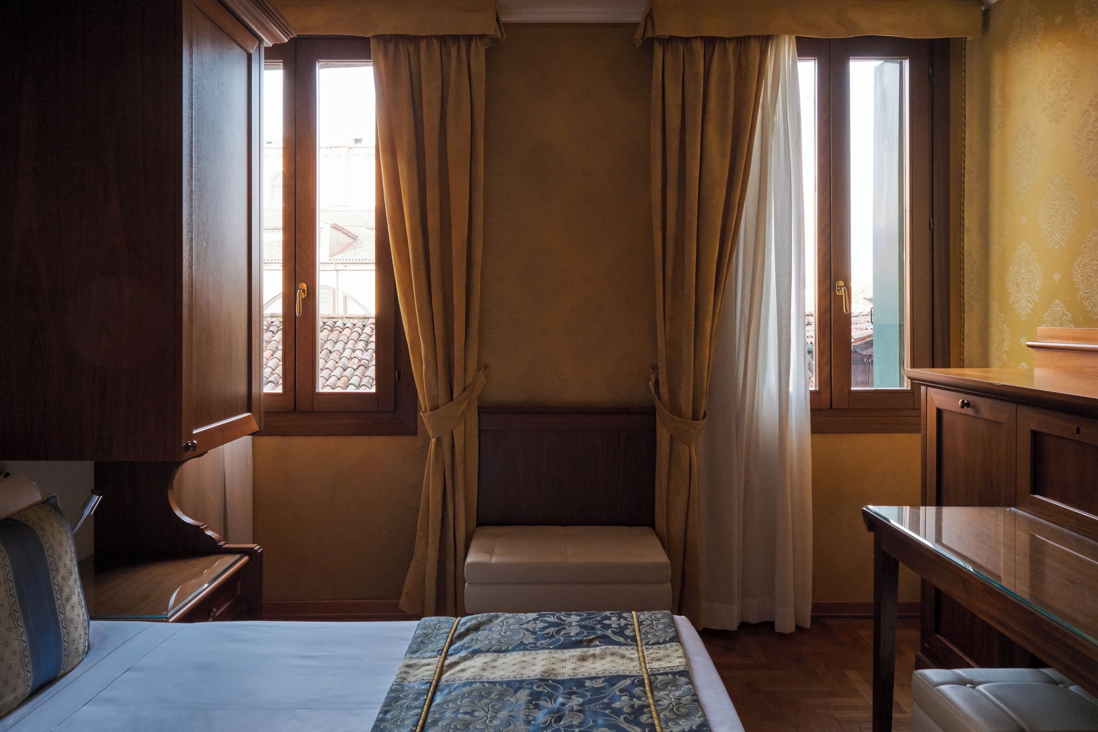 Una stanza con un letto, una panca, un tavolo e delle tende.