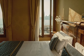 Une chambre d’hôtel avec un lit, des rideaux, une vue sur l’eau et un balcon doté d’une balustrade.