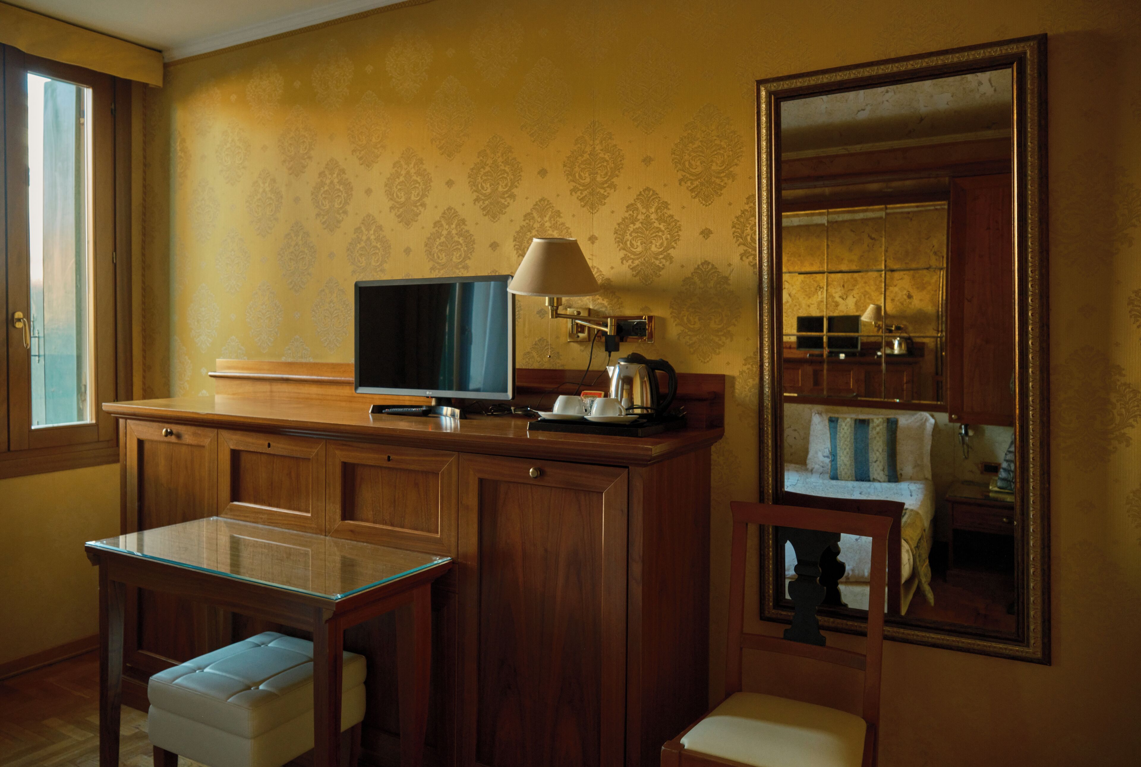 Habitación de hotel con un escritorio de madera, televisor, lámpara y espejo.