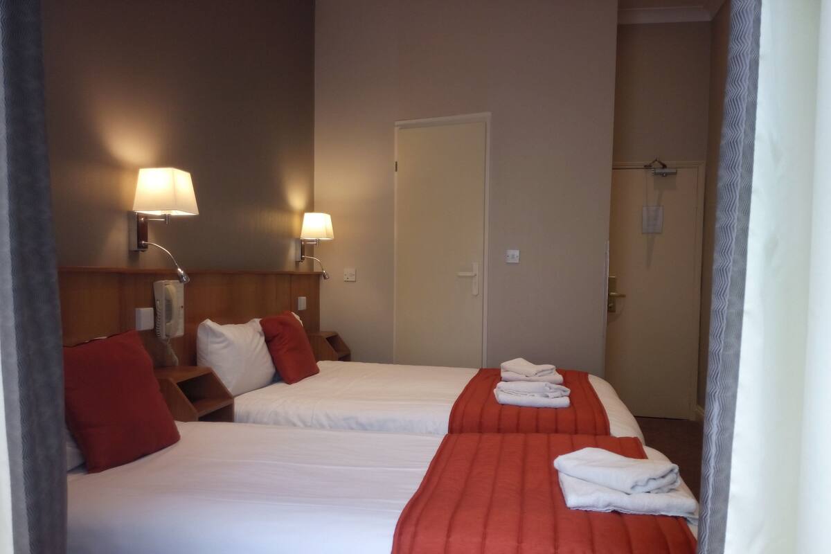 A hotel room with two beds, a wooden headboard, a telephone, and a wall-mounted lamp.