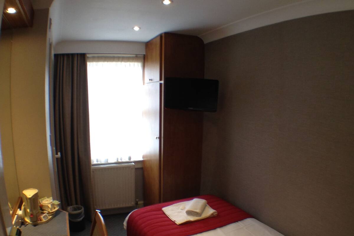 A hotel room with a bed, a desk, a chair, a TV, and a window with curtains.