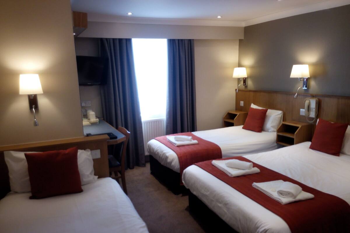 A hotel room with three beds, a desk, and a TV.