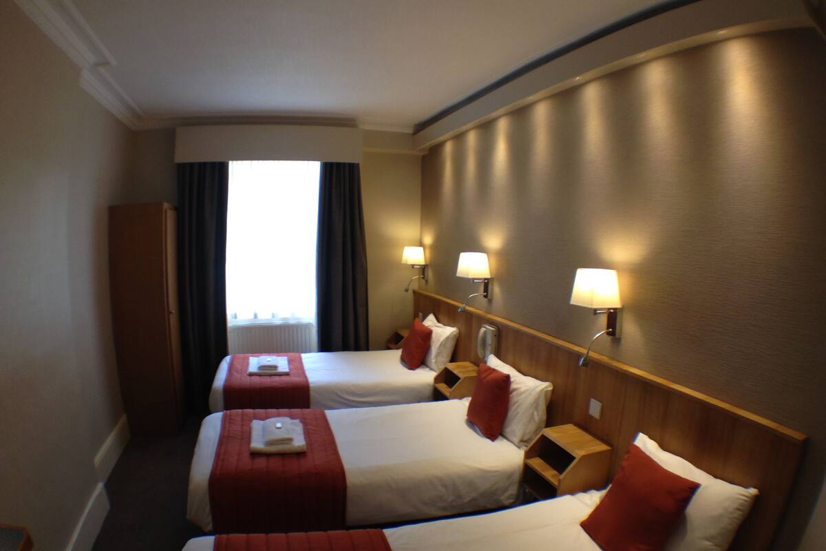 A hotel room with two beds, each with a red bedspread and white pillows, a wooden headboard, and a nightstand with a lamp.