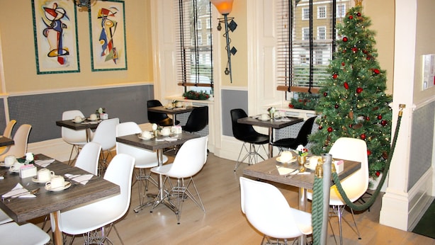 Un espace repas avec des tables et des chaises, un sapin de Noël et des œuvres d’art accrochées aux murs.