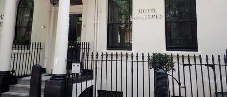 A building with a white facade, multiple windows, and a black metal fence.