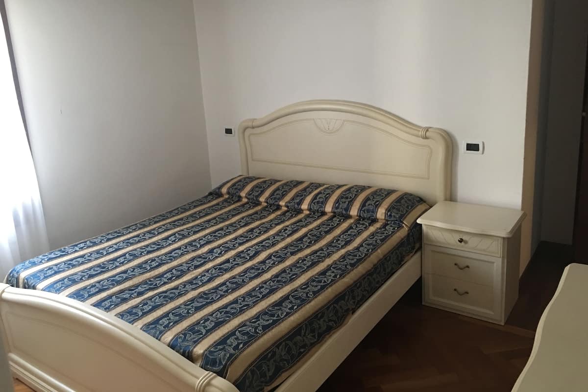 Una cama individual con una colcha estampada, una mesita de noche con cajones y una pared lisa.