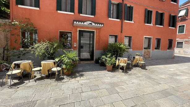 A building with a red facade, multiple windows with shutters, and outdoor seating with tables and chairs. - Albergo Marin (Venice)