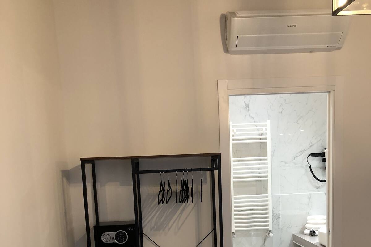 Un dormitorio con cama, un armario metálico negro con grafitis, y un baño con inodoro, lavamanos y espejo.