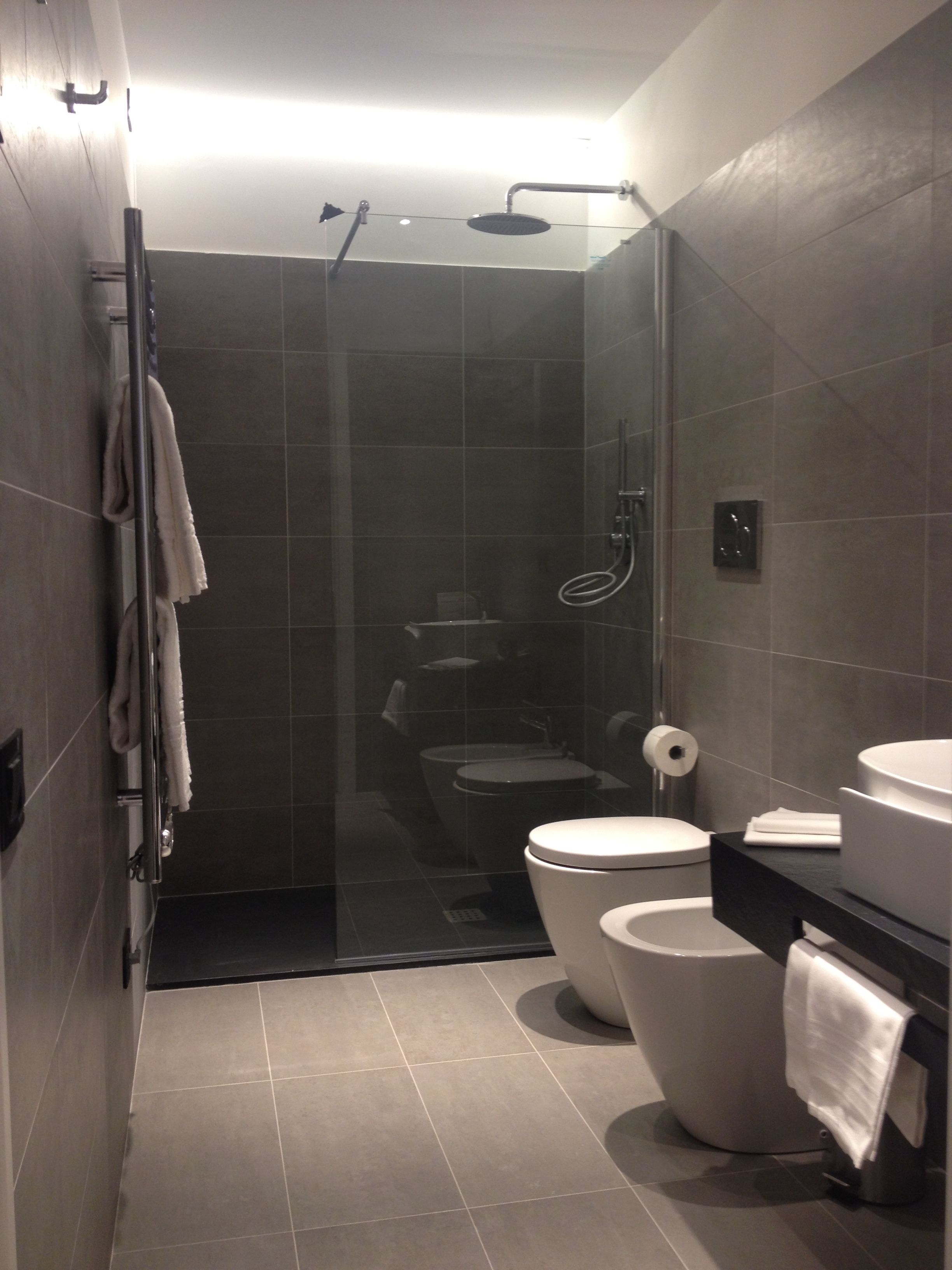 Un baño moderno con ducha de vidrio, dos inodoros, un lavamanos y un perchero para toallas.