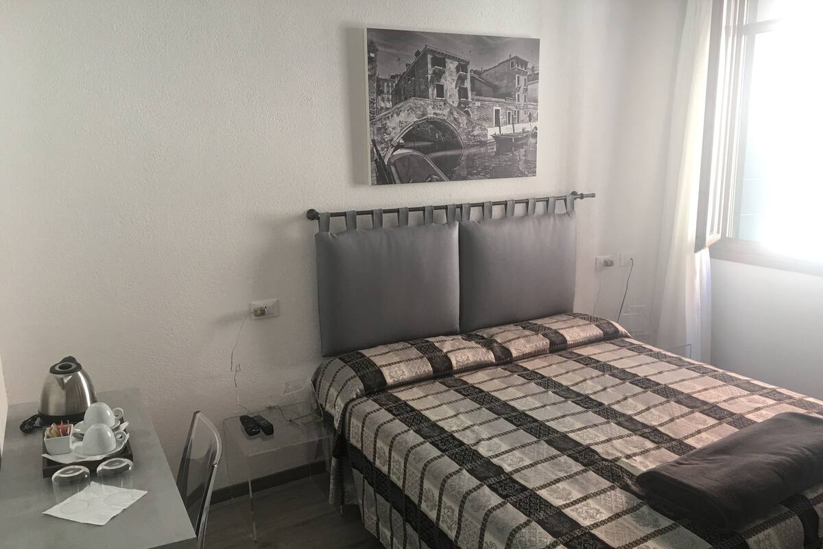 Habitación de hotel con cama, escritorio, hervidor, tazas y control remoto.