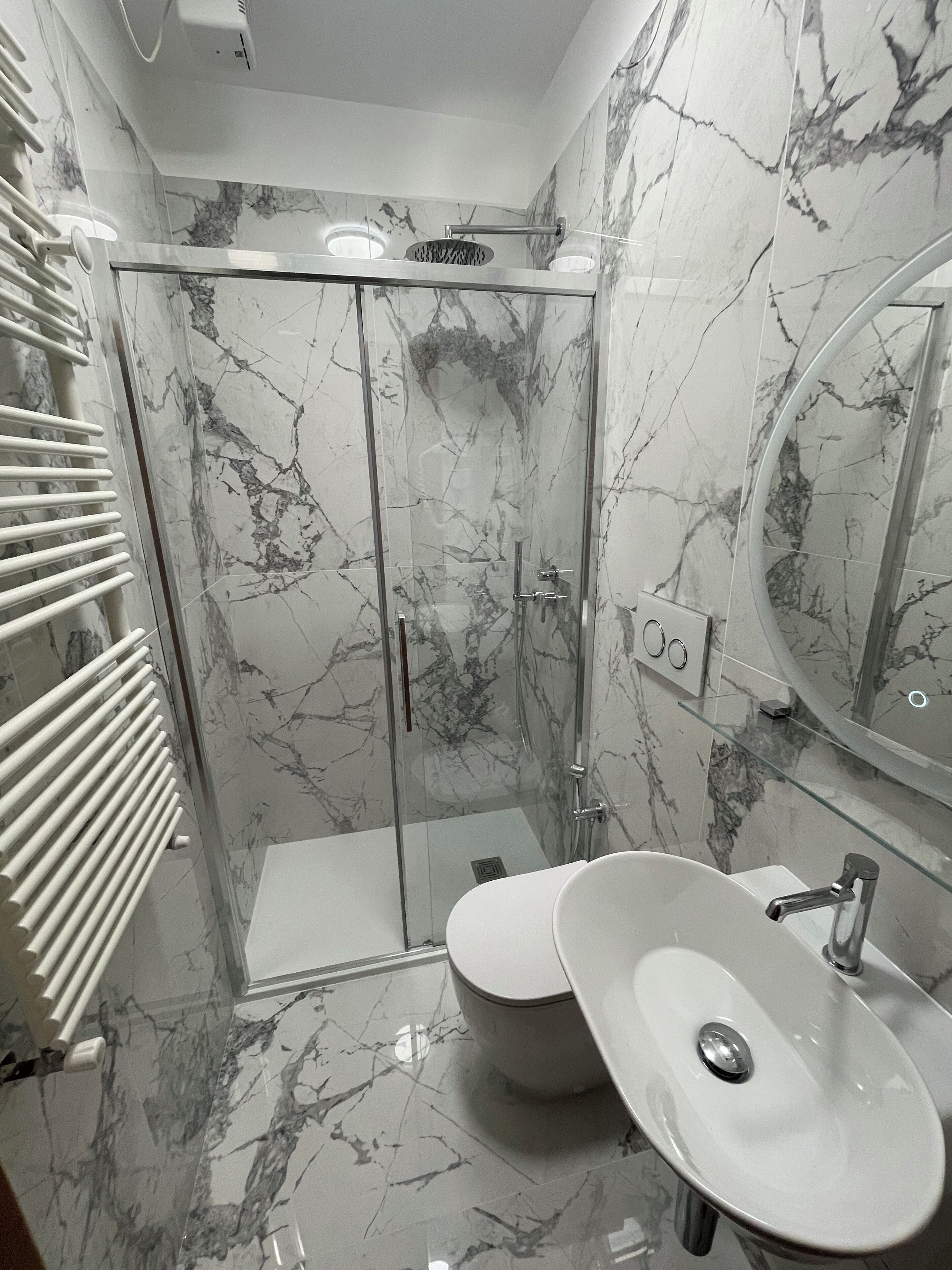 A modern bathroom with a glass-enclosed shower, a white sink, and a marble-tiled floor.