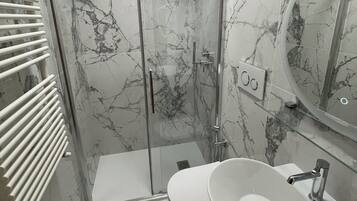A modern bathroom with a glass-enclosed shower, a white sink, and a marble-tiled floor.