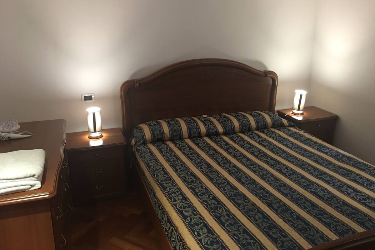Un dormitorio con cabecera de madera, colcha estampada y lámparas de noche.