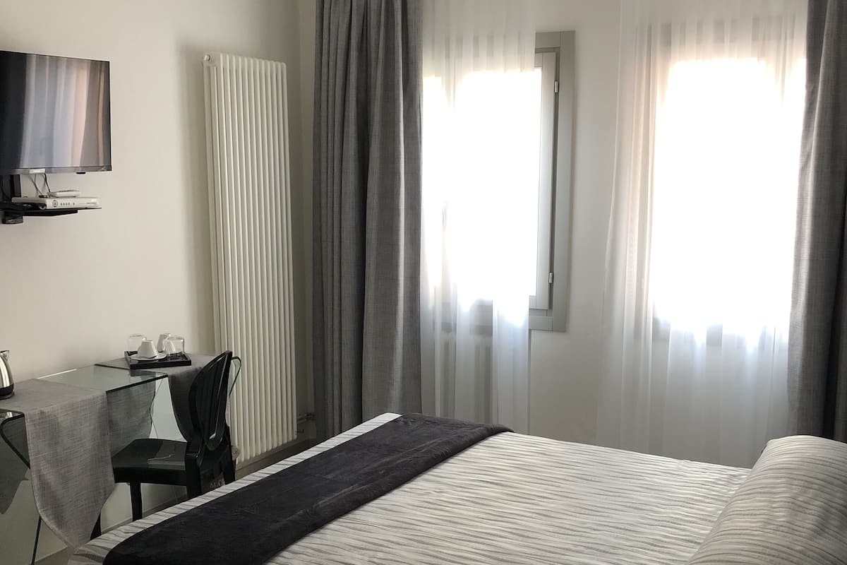 Habitación de hotel con cama, escritorio con silla, televisor y ventana con cortinas.