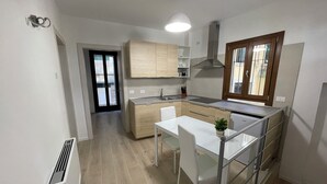 A modern kitchen with a dining area, featuring light wood cabinets, a stainless steel range hood, and a window with blinds. - Albergo Marin (Venice)