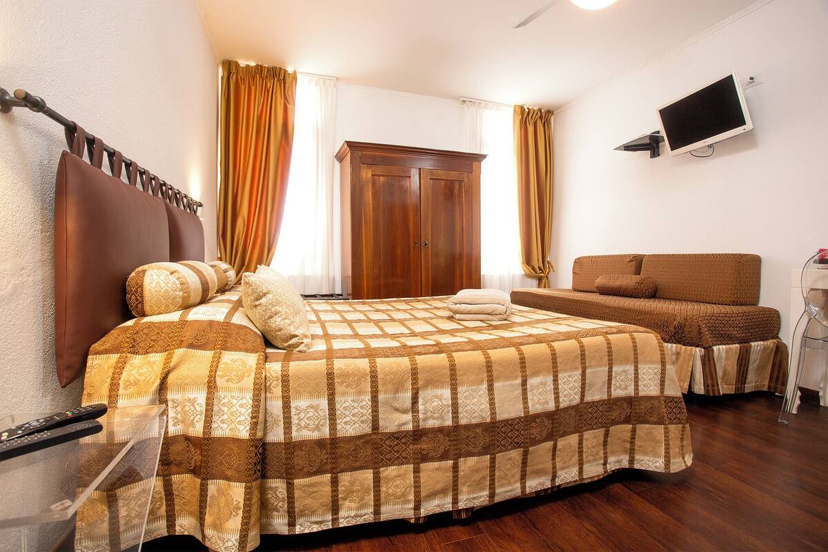 Un dormitorio con una cama, un sofá, un televisor montado en la pared y un armario.