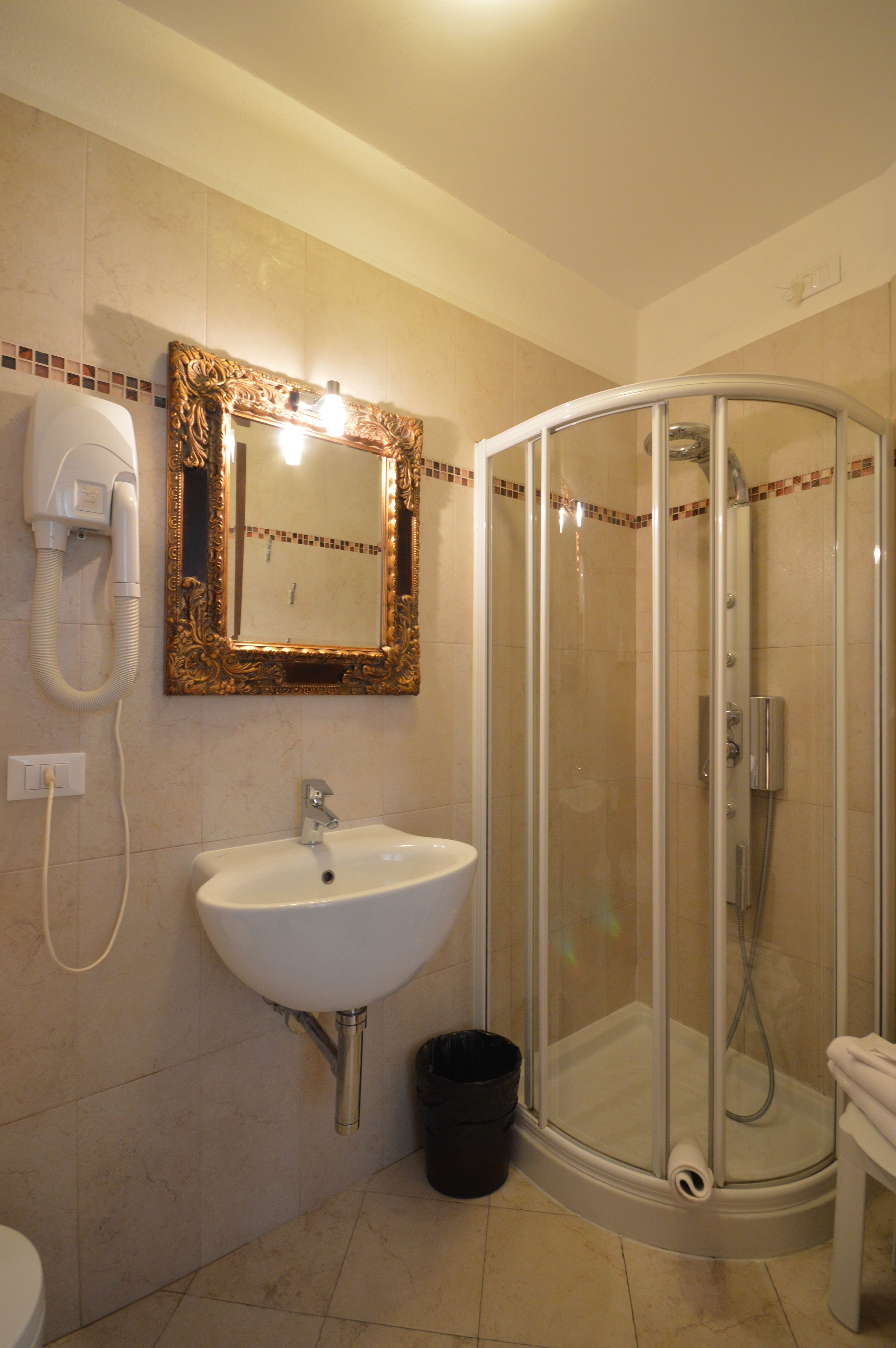 Een badkamer met een wit wastafel, een spiegel met een sierlijk frame, een douche met glazen wanden en een haardroger aan de muur.