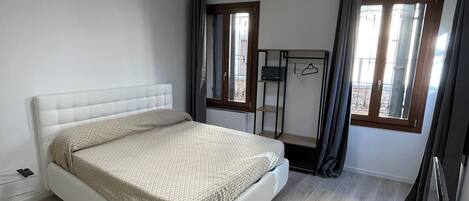 Un dormitorio moderno con una cama blanca, una lámpara de techo, un ventanal con cortinas y un televisor de pantalla plana.