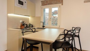 A compact kitchen with a microwave, a sink, and a window with a view of buildings. There are four chairs around a table. - Albergo Marin (Venice)